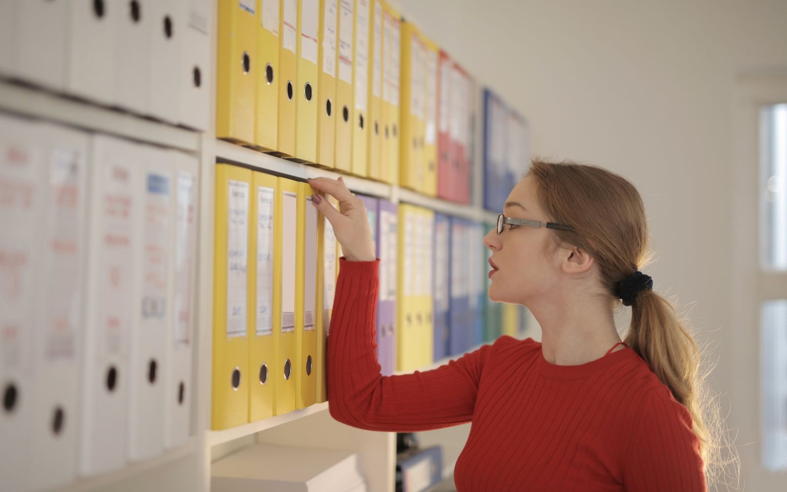 Une comptable cherche un dossier parmi des classeurs pour repérer un doublon de facture